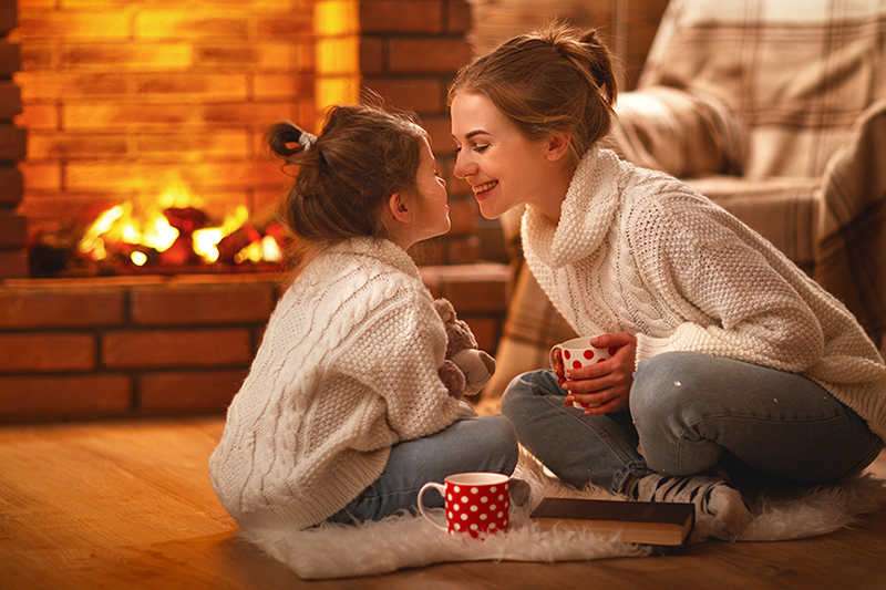 Mother and daughter enjoying hot cocoa by the fireplace.